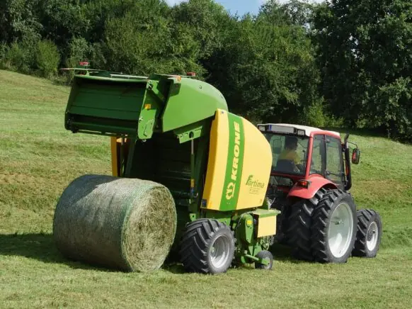 Rød traktor med Krone Fortima rundballepresser som slipper ut en fersk rundballe på jordet.