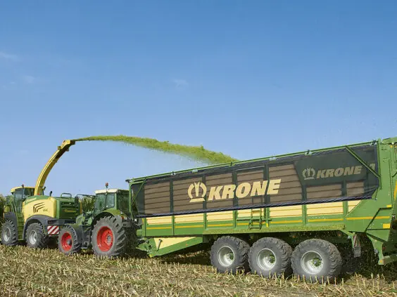 Fôrhøster fyller en grønn og gul KRONE TX lessevogn med fôr på maisåkeren.