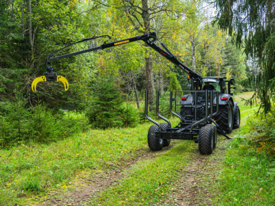 Traktor med Palms 5.87z skogskran og tømmertilhenger på en grønn skogsvei.