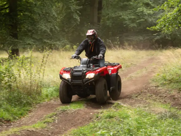Rød Honda TRX420 ATV i kjøring på jordsti gjennom gress