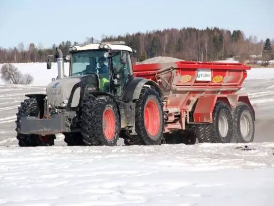 En grå Fendt-traktor med rød kalkspreder kjører på et snødekket jorde om vinteren.