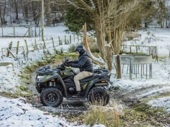 Grønn Kymco MXU 550i i kjøring på gård med snø