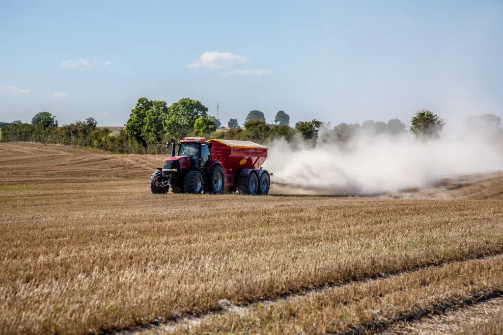 Rød traktor sprer kalk på en høstet åker og etterlater en stor støvsky.