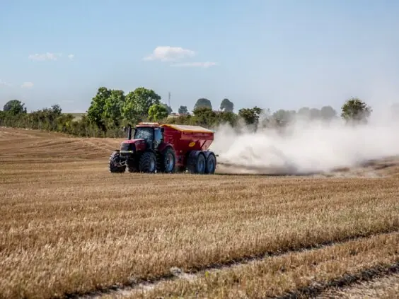 Rød traktor sprer kalk på en høstet åker og etterlater en stor støvsky.