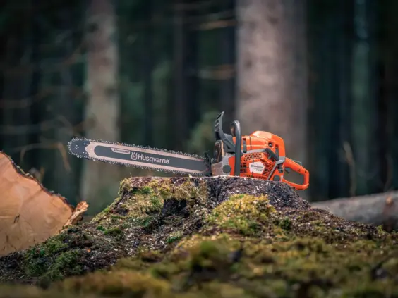 En oransje Husqvarna motorsag plassert på en mosegrodd trestubbe i en dyp skog.