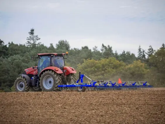 Blå DALBO Cultitrail såbedsharv utfoldet i arbeid bak en rød traktor på pløyd jord.