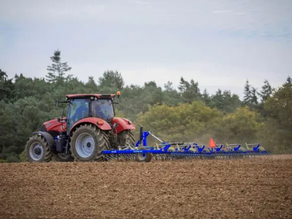 Blå DALBO Cultitrail såbedsharv utfoldet i arbeid bak en rød traktor på pløyd jord.