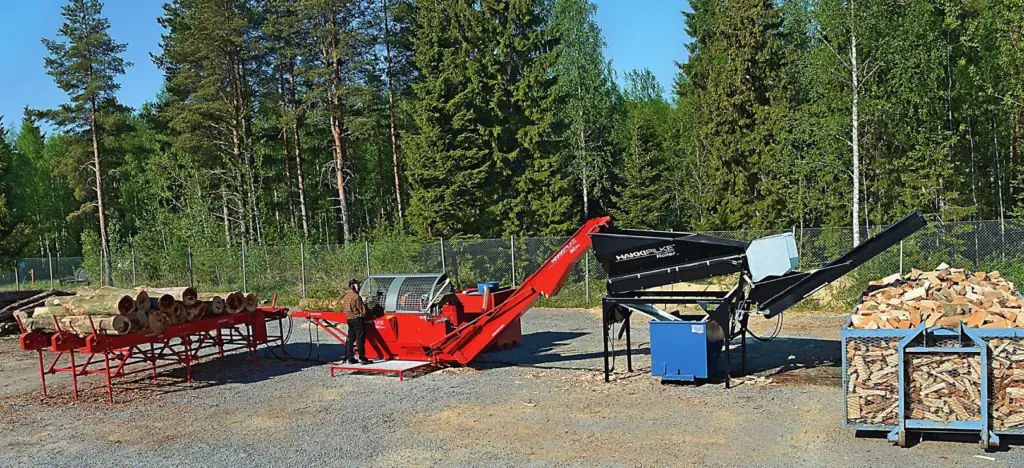 Hakki Pilke 50 Pro vedmaskin i drift på en gårdsplass, med stokkebord, operatør, vedrenser og ferdig ved i kasser.