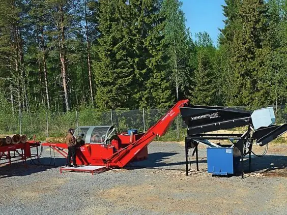 Hakki Pilke 50 Pro vedmaskin i drift på en gårdsplass, med stokkebord, operatør, vedrenser og ferdig ved i kasser.