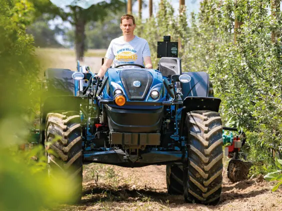 Fører på New Holland T4 LP mellom trerekkene i en frukthage