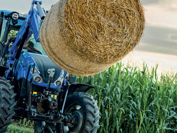 New Holland T5S med rundball på frontlasteren ved en maisåker