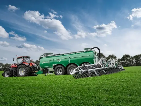 Traktor med grønn SAMSON TG gjødselvogn og TSB2 stripespreder med slepesko på en eng.