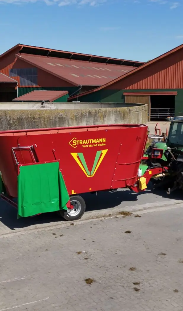 Strautmann Verti-Mix fullfôrvogn koblet til traktor på gårdsplassen foran driftsbygningen