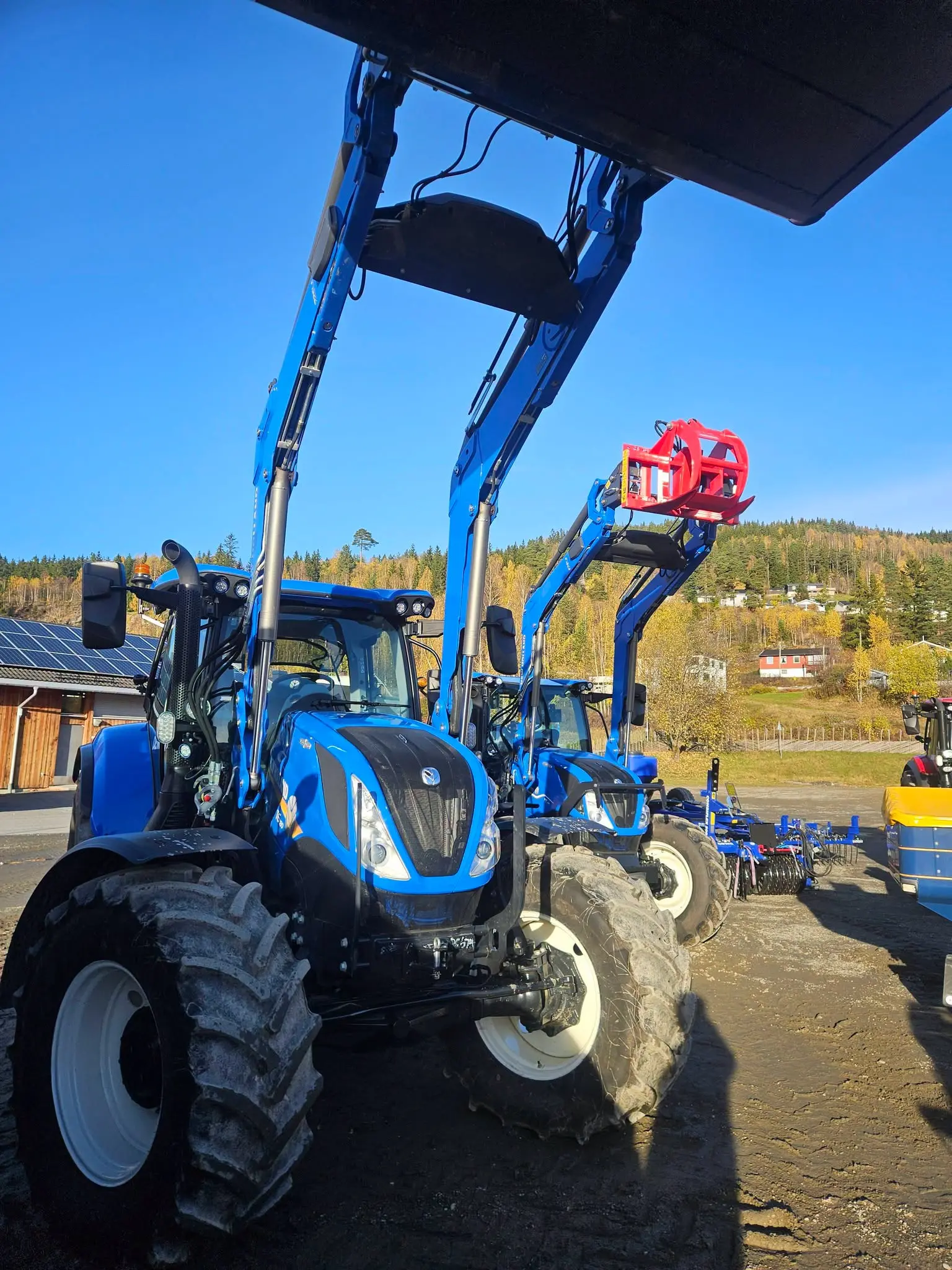 Blå New Holland-traktor med frontlaster og hevet skuffe utstilt på Stavsmartn på Tretten.