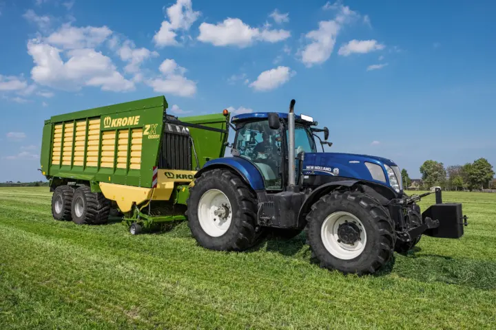 New Holland T7.270 med KRONE ZX 430 GD lessevogn på nyslått eng under blå himmel med sommerskyer